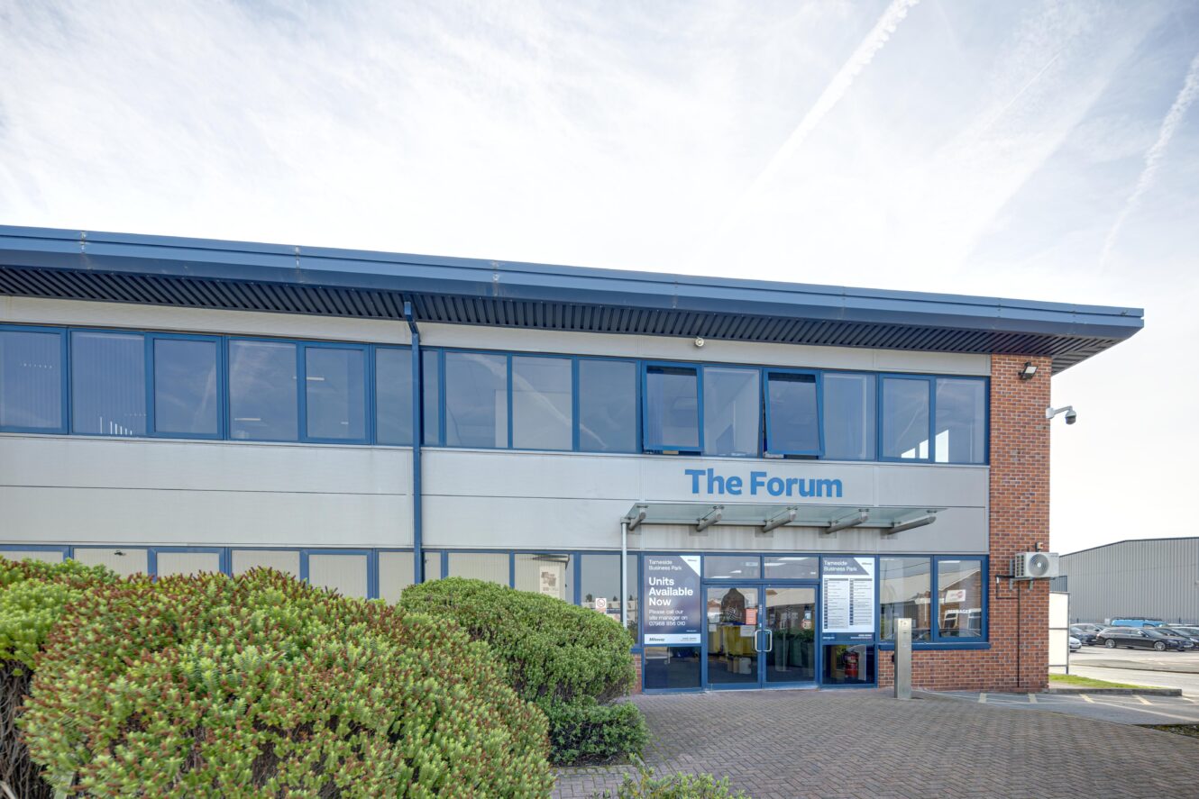 Exterior view of a modern two-storey office building labelled The Forum, featuring large windows, a glass entrance, and bushes in the foreground.