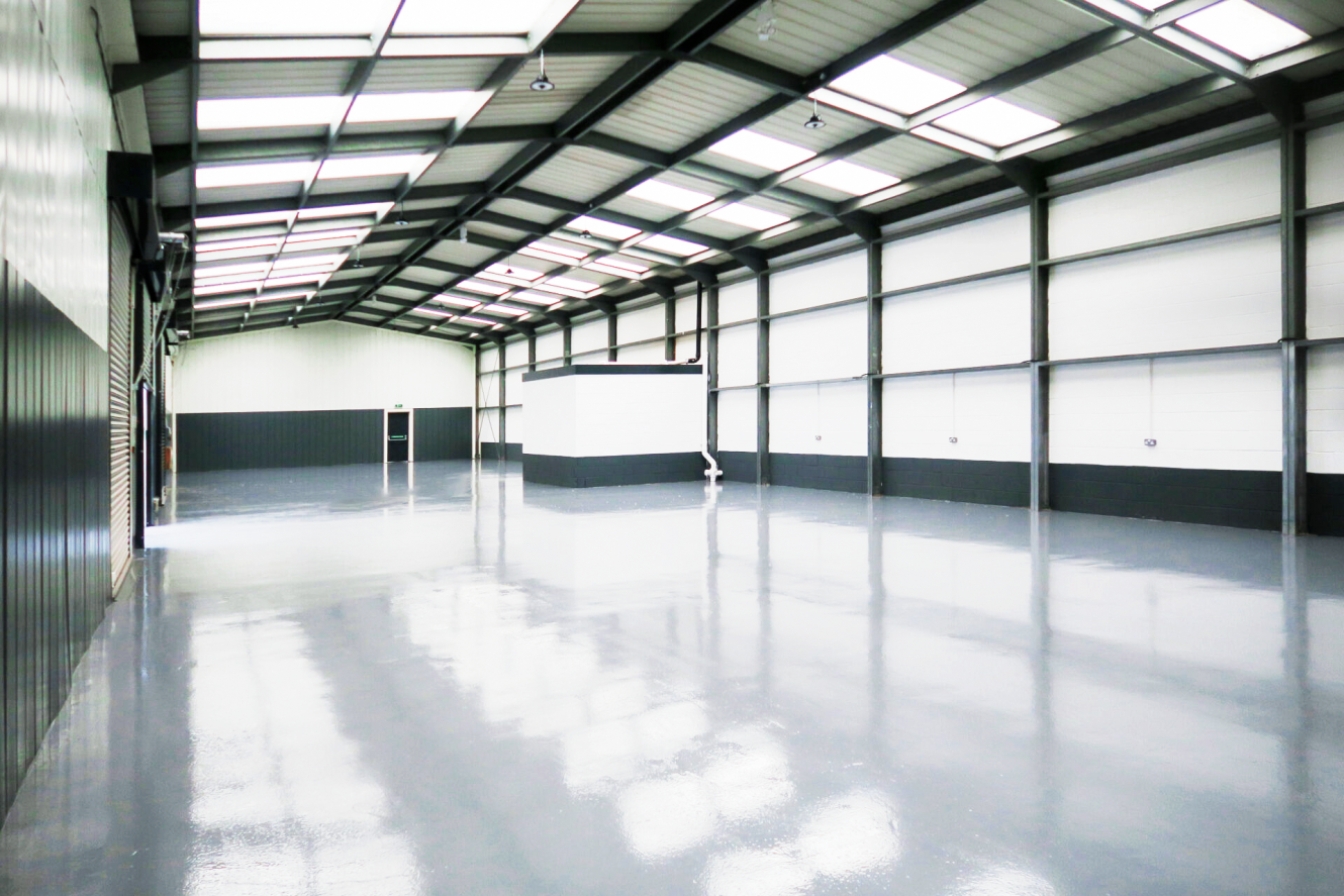 Interior of an empty, modern warehouse with polished concrete floors, high ceiling, skylights, and white and black walls.