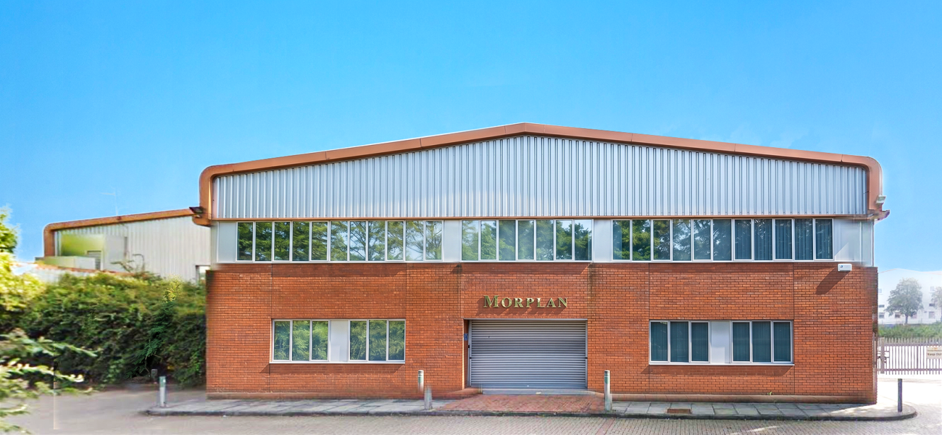 A large industrial building with a red brick facade, upper metal cladding, many windows, and a central metal roller door under the sign J.A. ORPEAN on a paved yard.