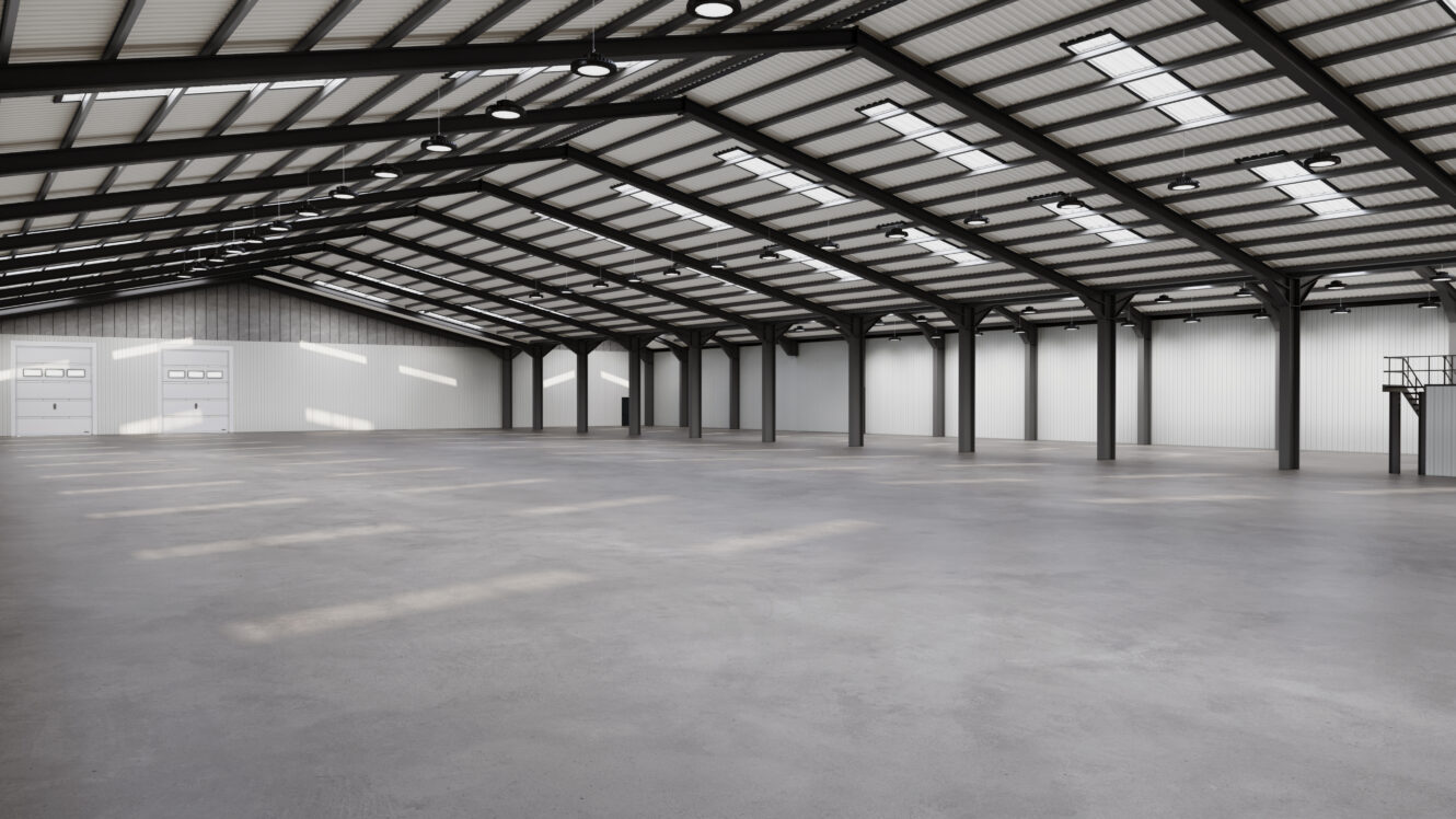 Spacious empty warehouse with a high ceiling, large windows, and a concrete floor. The interior features steel beams and white walls, with two large doors visible at the far end.