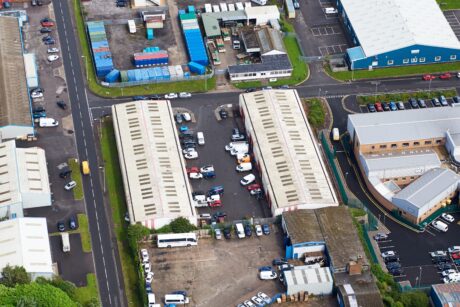 Aerial view of an industrial area with warehouses, parked cars, lorries, and surrounding roads.