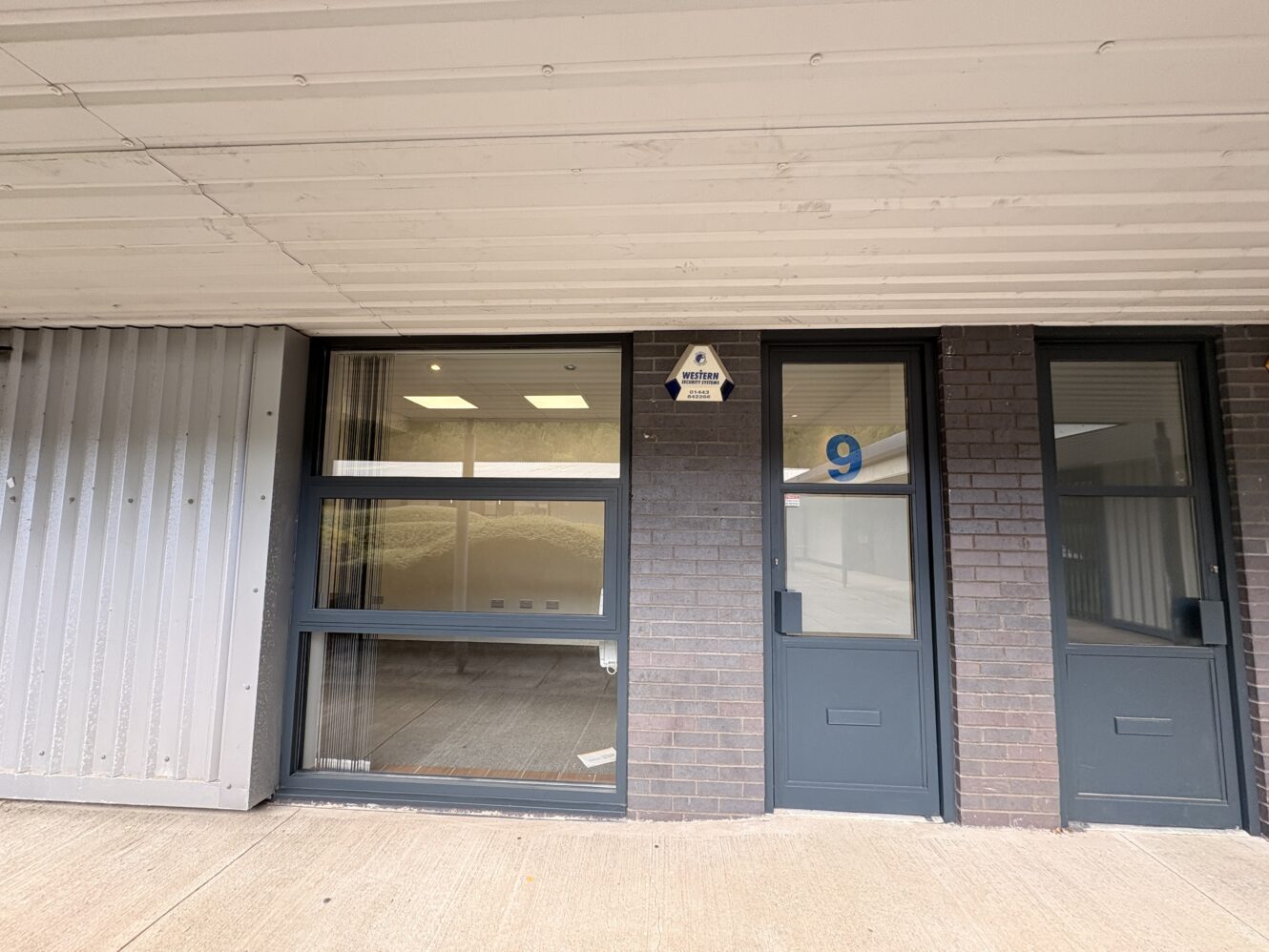 Exterior view of a building with a glass window and a door labelled with the number 9; a small sign above the door reads West End Offices.