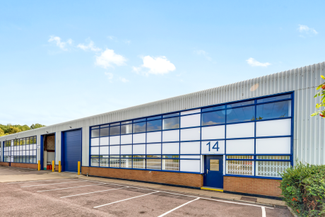 Exterior of a modern industrial warehouse unit with large blue-framed windows, labelled number 14, and an empty car park in front.