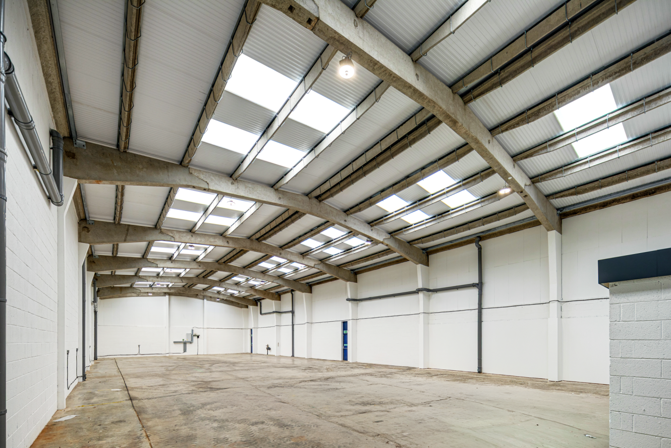 Empty warehouse interior with a concrete floor, white walls, and a vaulted ceiling with skylights.