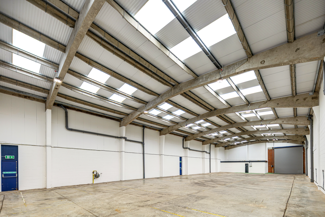 Large empty industrial warehouse with white walls, a concrete floor, and skylights set into a pitched roof.
