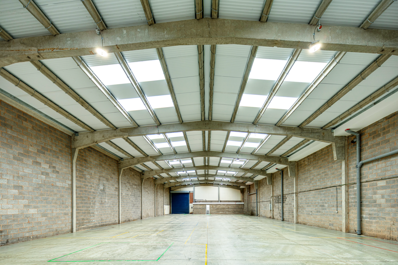 An empty, high-ceilinged industrial warehouse space with concrete block walls, a polished concrete floor, and skylights along the arched roof.