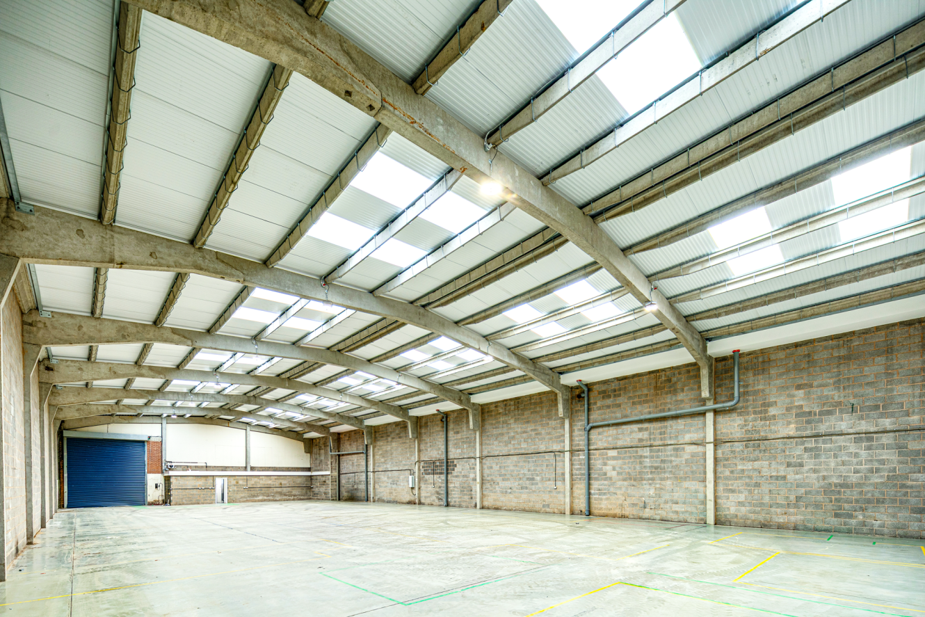 Empty warehouse with a concrete floor, grey brick walls, and a pitched roof featuring integrated rooflights.