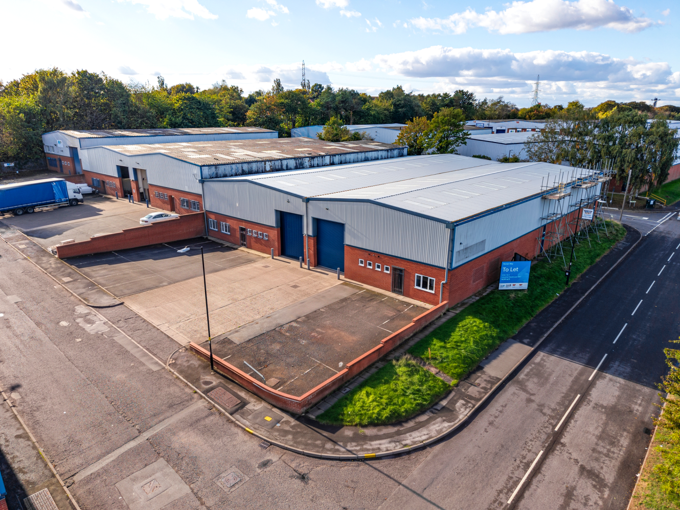 Aerial view of a commercial industrial estate with warehouse buildings, parking areas, and a To Let sign.