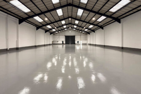 An empty, spacious warehouse with a high vaulted ceiling, white walls, and a polished grey floor.