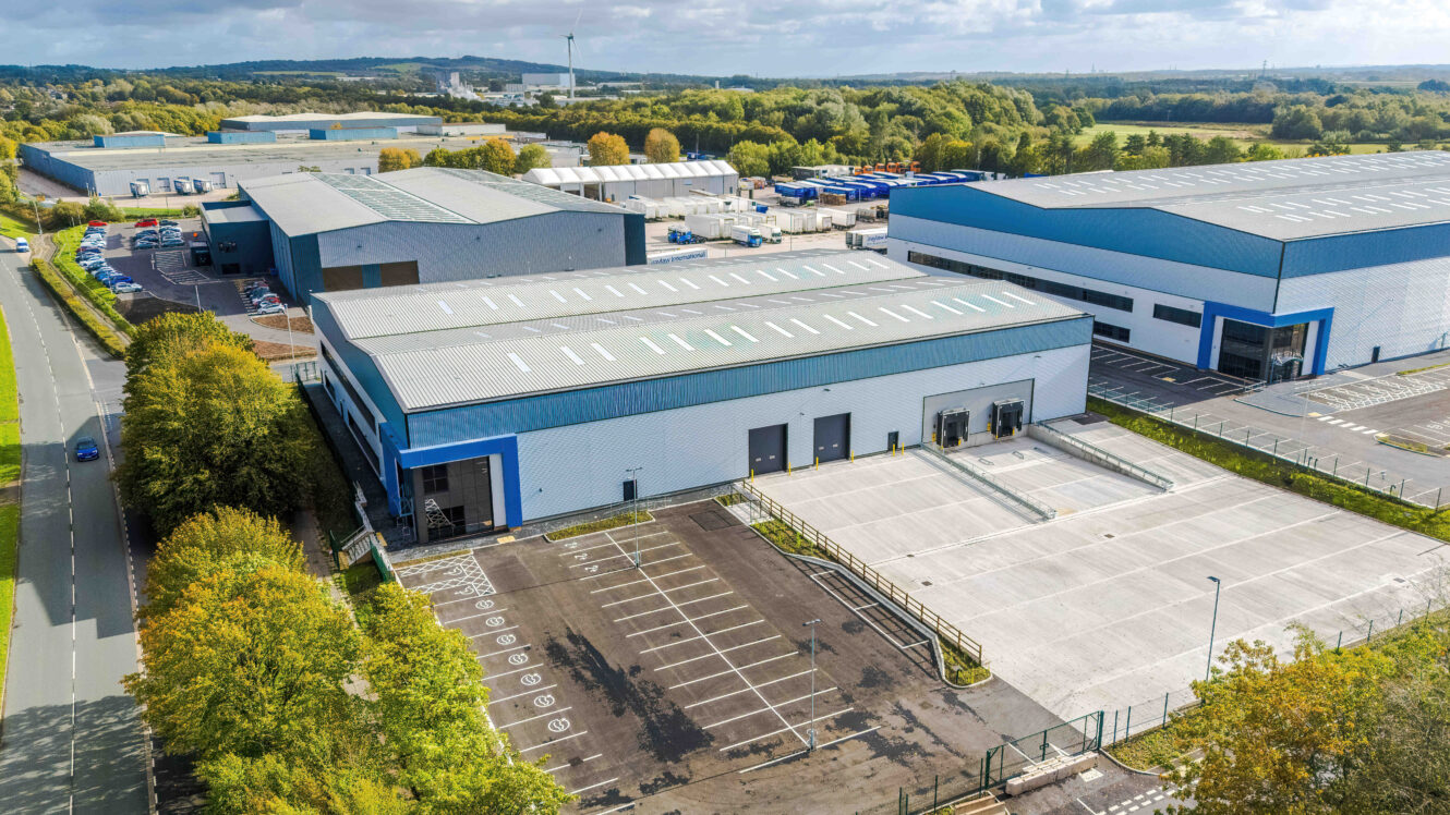 Aerial view of a large industrial warehouse complex with loading bays, paved car parks, and surrounding green space.
