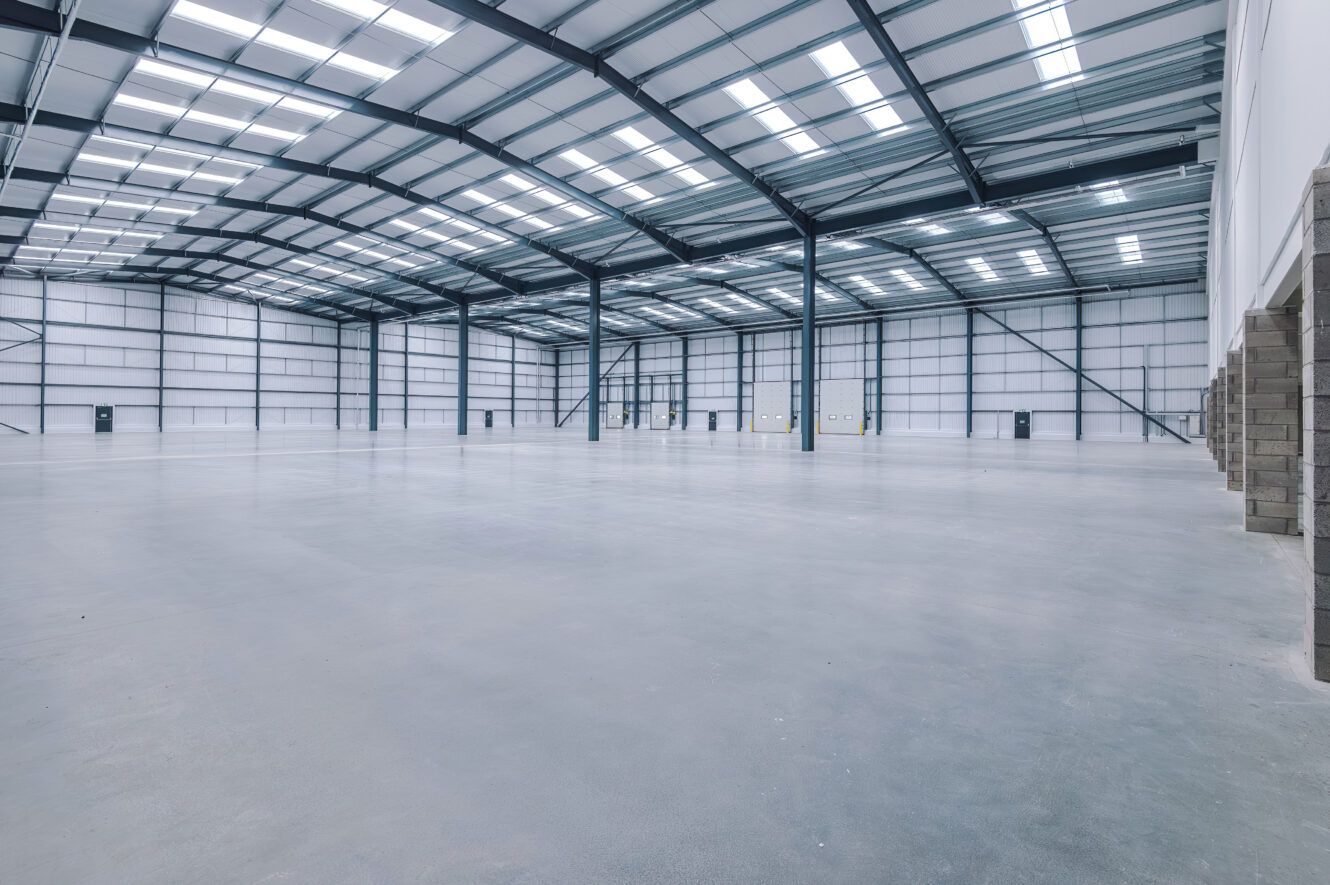 Empty industrial warehouse interior with a concrete floor, metal walls, and a high-pitched ceiling with rooflights.