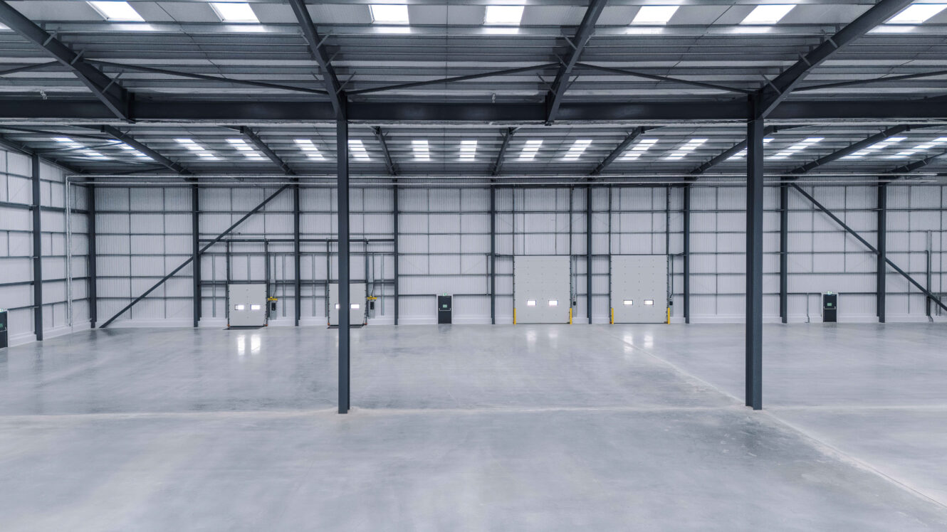 Empty warehouse interior with high ceilings, concrete floors, and metal loading bay doors.