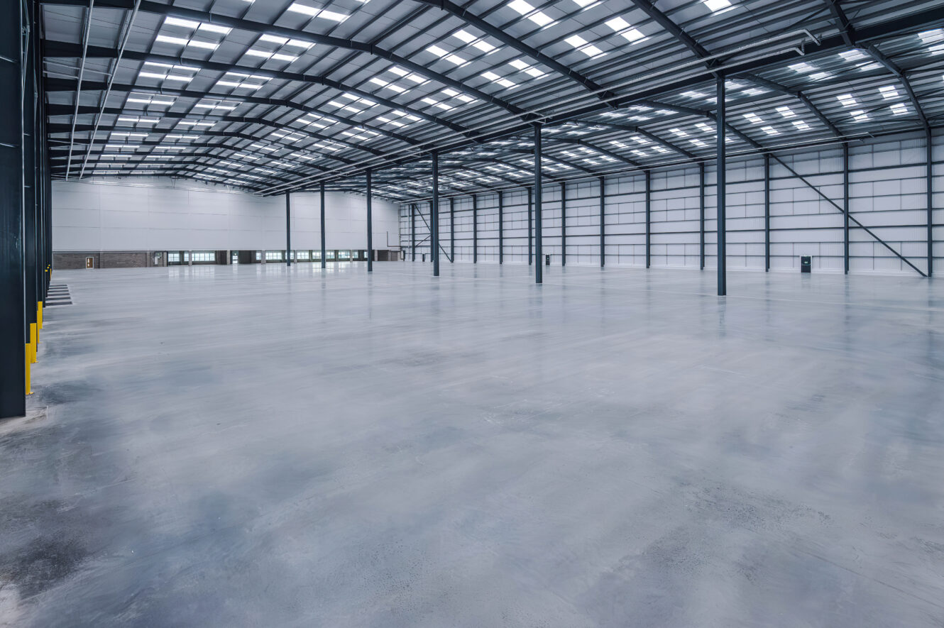 Large, empty industrial warehouse with high ceilings, concrete floors, and metal support columns.