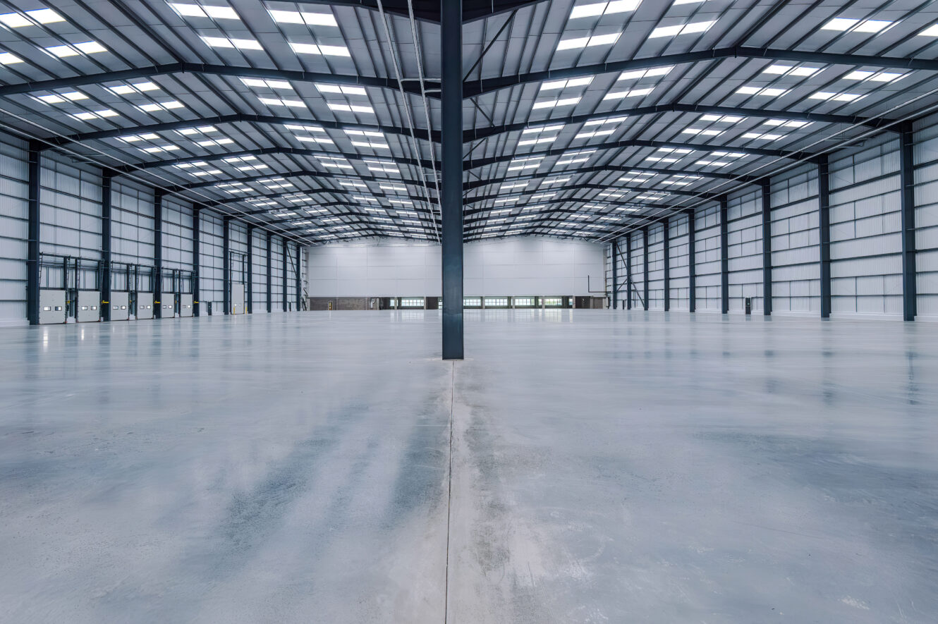 An expansive, empty industrial warehouse with a high gabled ceiling and a large central support pillar.