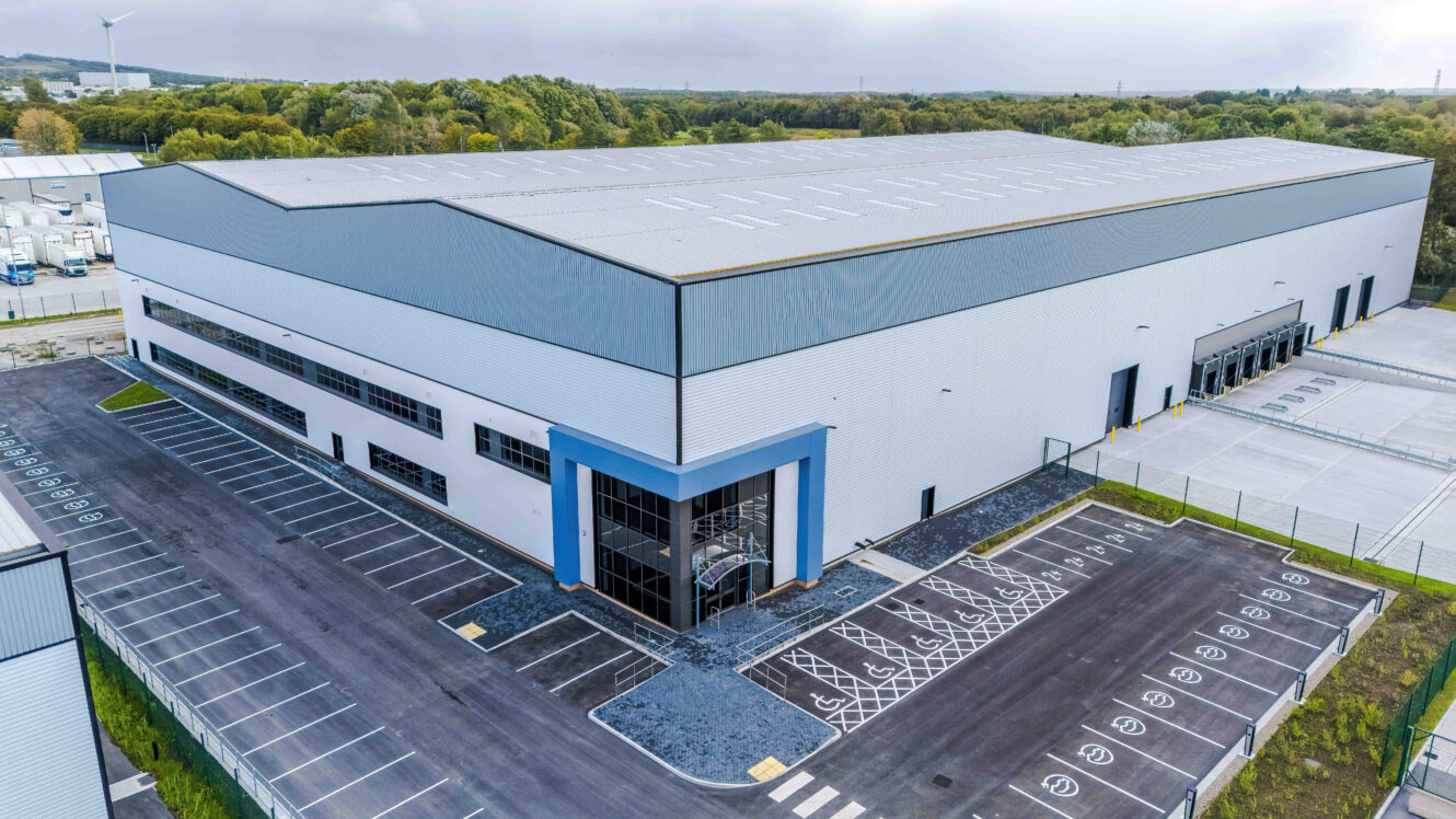 Aerial view of a large modern warehouse with a car park and loading bays.