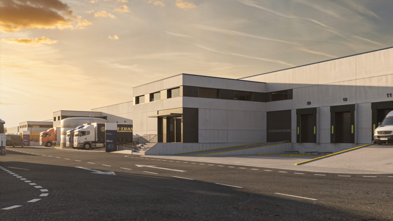 Almacén moderno con muelles de carga, varios camiones aparcados o siendo cargados, y un cielo despejado al atardecer.