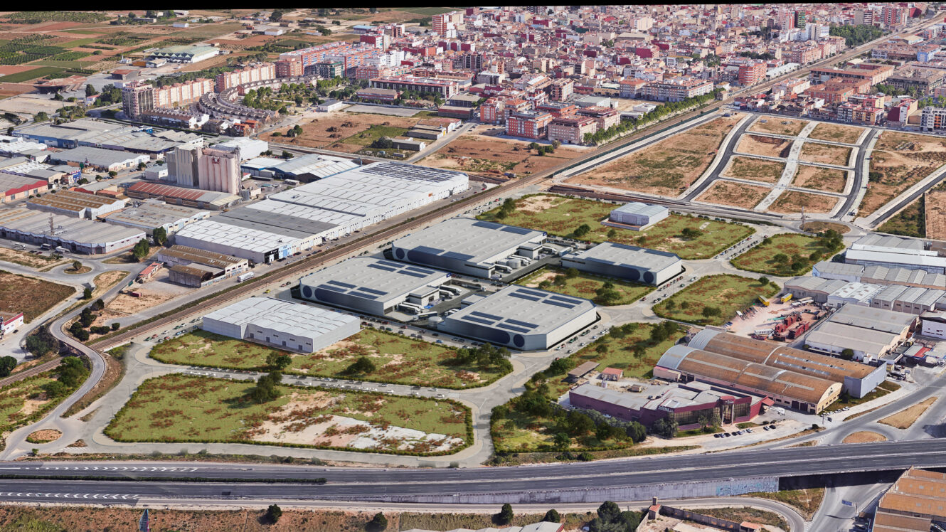 Vista aérea de una zona industrial con almacenes, zonas verdes circundantes y una zona residencial urbana cercana al fondo.
