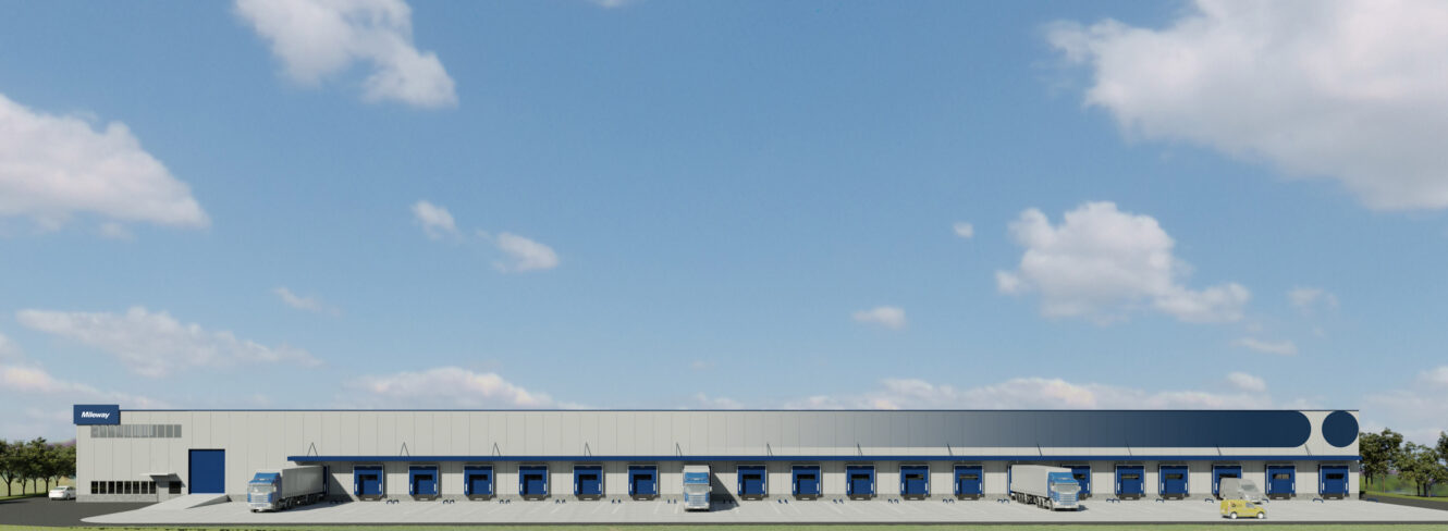 Un grande edificio adibito a magazzino con diverse banchine di carico, diversi camion parcheggiati nelle baie e un cielo limpido in alto.