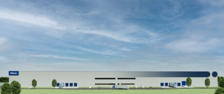 Un grande magazzino moderno con banchine di carico, un camion, diverse auto, alberi e un cielo blu con nuvole sparse.