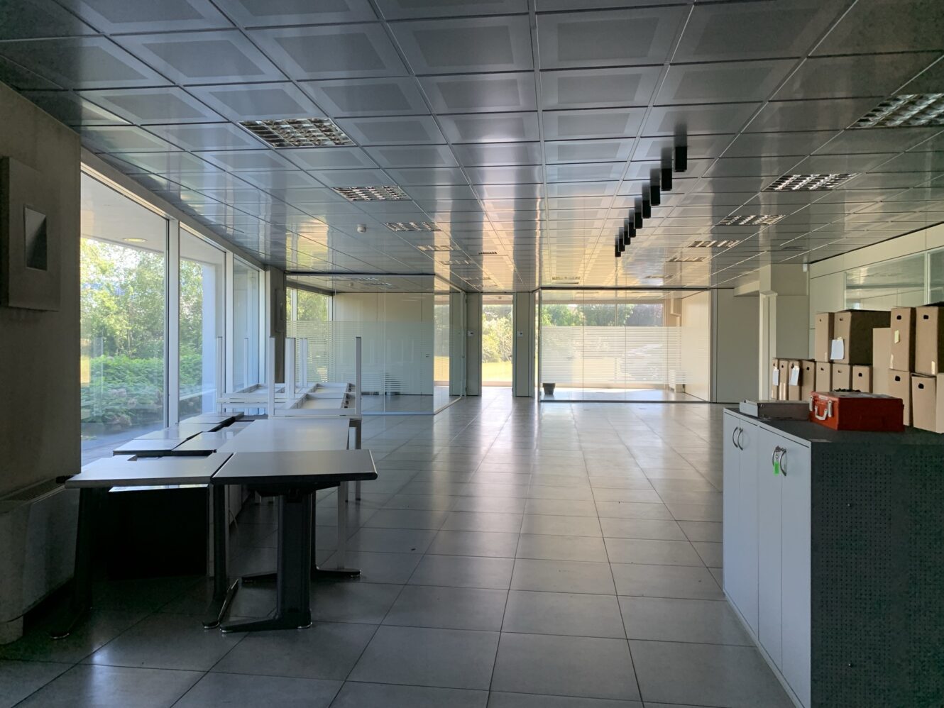 Un moderno ufficio vuoto con grandi finestre, scrivanie, sedie, pavimenti piastrellati, plafoniere e scatole di cartone vicino all'ingresso.