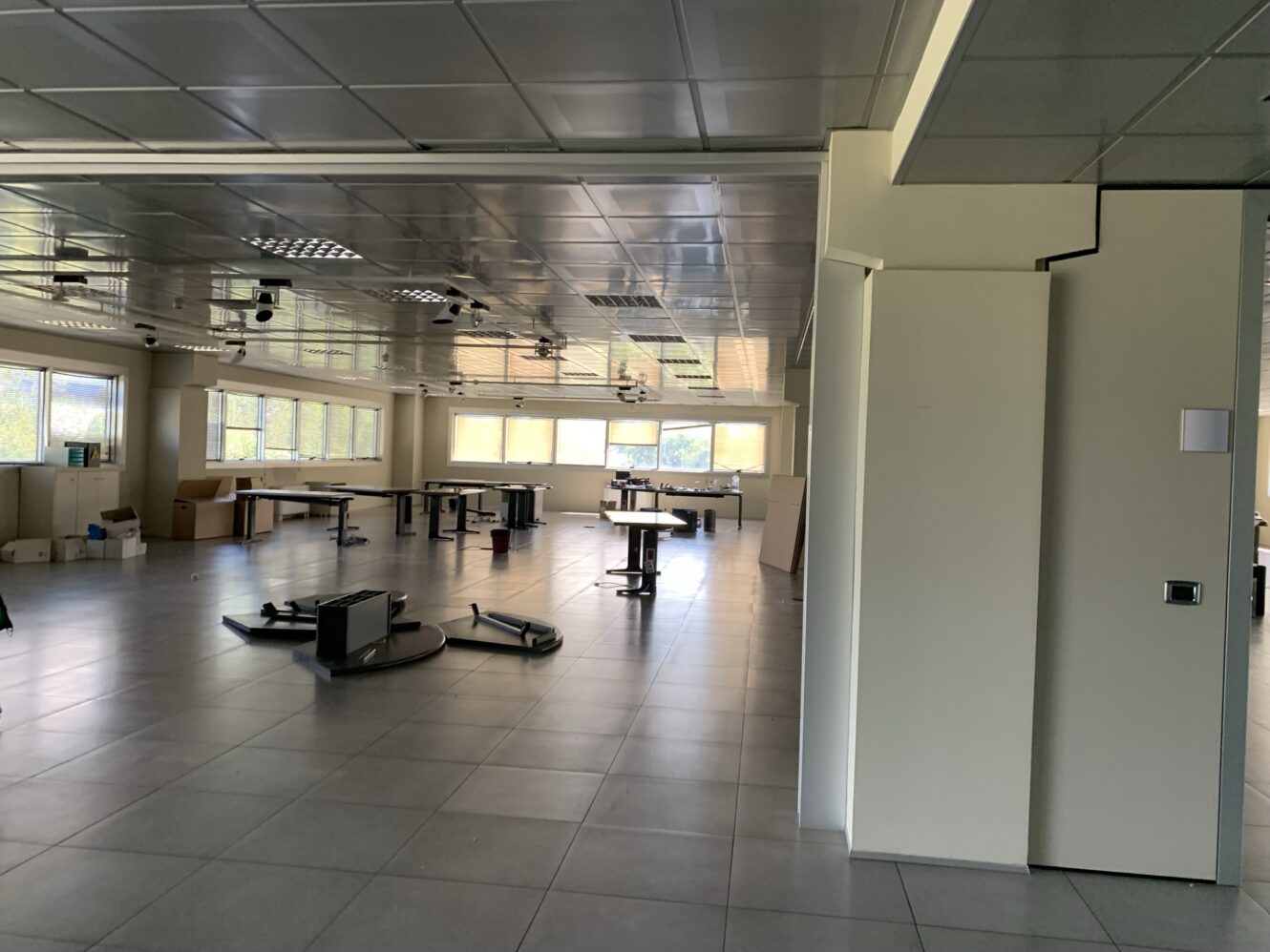 Un grande ufficio, per lo più vuoto, con sedie rovesciate, scrivanie smontate e scatoloni vicino alle finestre, sotto un soffitto a griglia con luci fluorescenti.