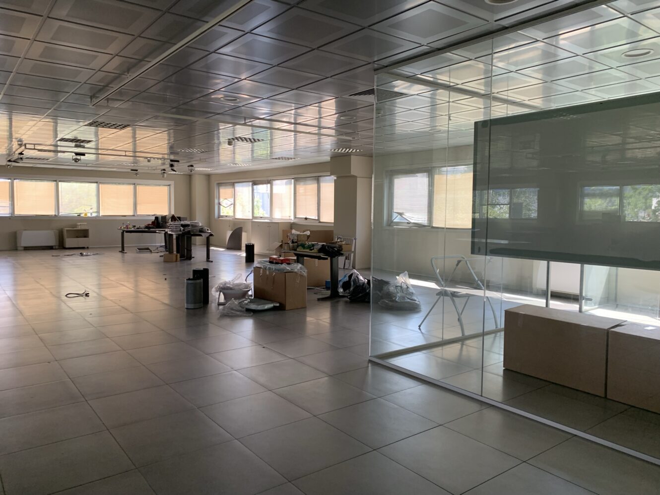 Un ufficio spazioso e moderno, con grandi finestre, pareti di vetro e scatoloni disfatti sparsi in giro, che indicano un trasloco recente o un allestimento in corso.