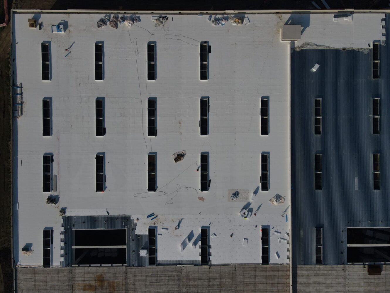 Vista aerea di un tetto bianco e piatto con diversi lucernari rettangolari e materiali da costruzione sparsi.