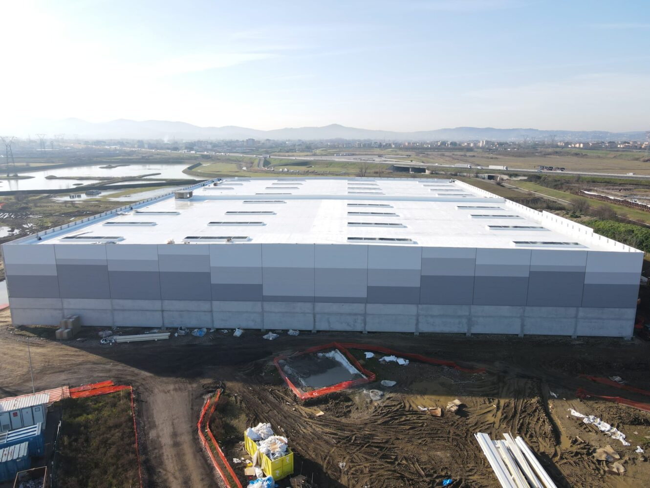 Un grande e moderno capannone industriale in costruzione con materiali da costruzione e attrezzature sparse per il sito.