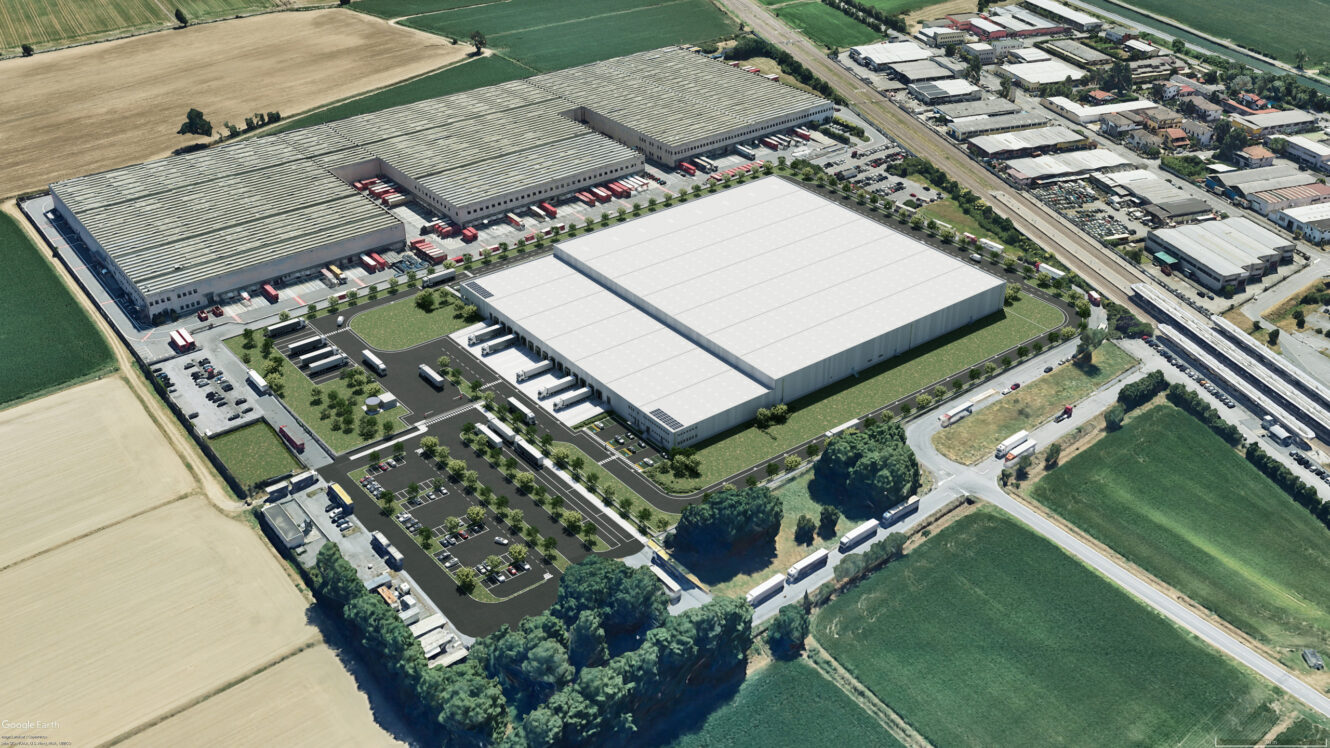 Vista aerea di un grande impianto industriale con diversi magazzini, parcheggi, camion per le consegne e campi verdi circostanti.