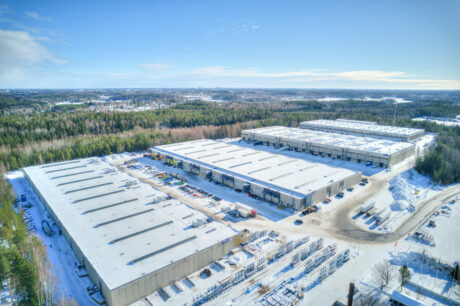 Ilmakuva suurista varastoista ja teollisuusrakennuksista lumen ja metsäalueiden ympäröimänä kirkkaalla taivaalla.