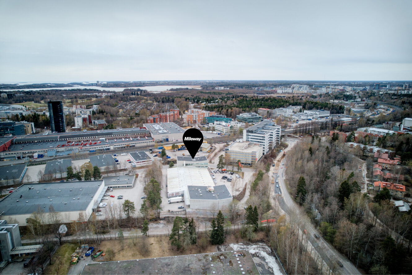 Ilmakuva teollisuus- ja asuinalueesta, jonka keskellä on Midwayn sijaintimerkki, puiden ja rakennusten ympäröimänä pilvisen taivaan alla.