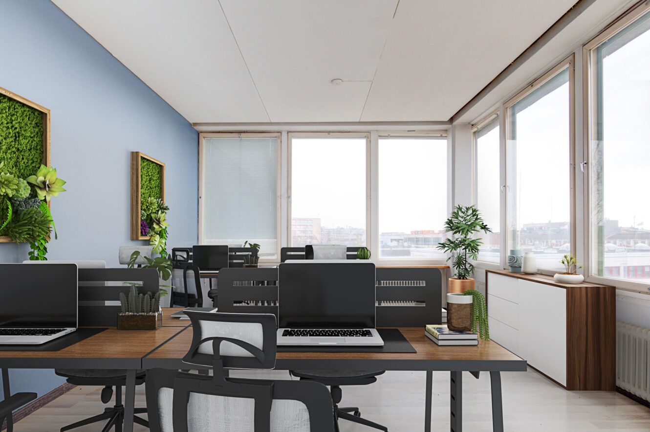Moderni toimistotila, jossa on useita työpöytiä, mustia tuoleja, kannettavia tietokoneita, ruukkukasveja, suuret ikkunat ja kehystetty vihreä seinätaide. Luonnonvalo täyttää huoneen.