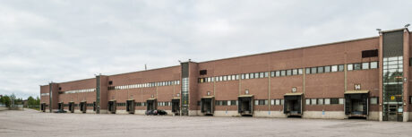 Suuri, tyhjä lastauslaiturialue, jossa on useita lastauslaitureita numeroilla 11-14 ruskeassa teollisuusvarastorakennuksessa pilvisen taivaan alla.