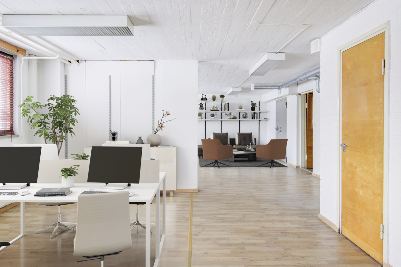 Moderni avokonttori, jossa on valkoisia pöytiä, tietokoneita, ruukkukasvi ja oleskelutila, jossa on ruskeita tuoleja ja hyllyjä taustalla.