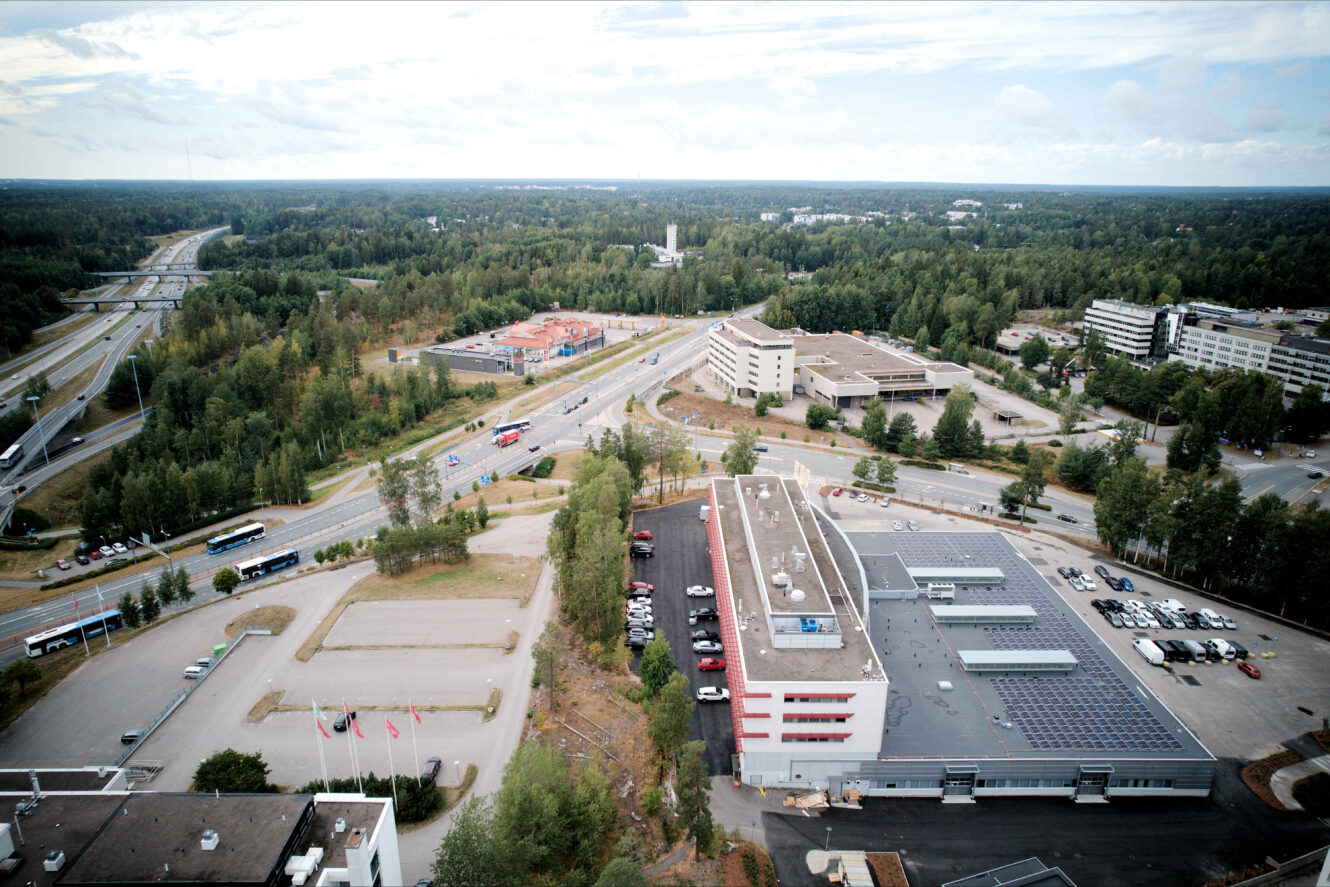 Ilmakuva teollisuus- ja toimistokompleksista, jota ympäröivät tiet, pysäköintialueet ja metsäalueet osittain pilvisen taivaan alla.