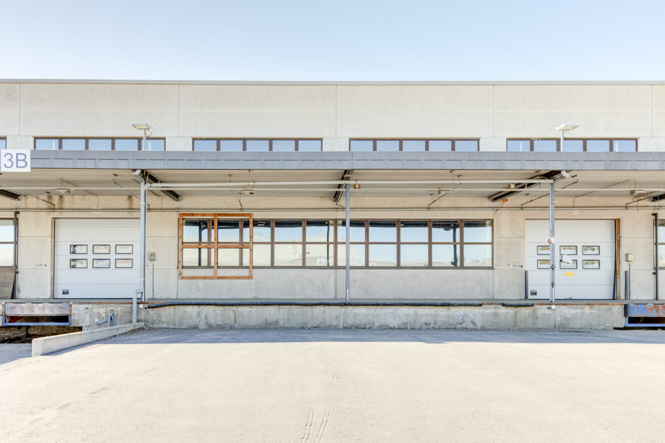 Lastauslaituri, jossa on suljetut ovet, betonilava ja ulkoneva metallikatto, kevyen teollisuusrakennuksen ulkopuolella kirkkaana päivänä.