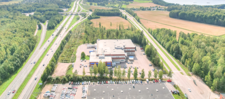 Ilmakuva liikerakennuksesta ja suuresta pysäköintialueesta, jota ympäröivät tiet, valtatiet ja vihreät pellot maaseudulla.
