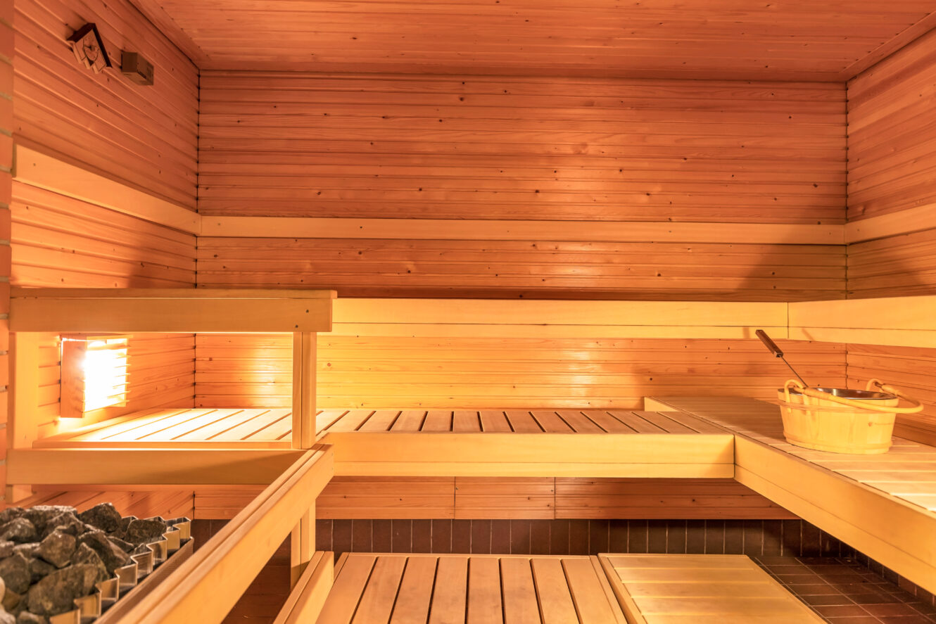 Puisen saunan sisätilat, joissa on porrastetut lauteet, kauha ja kauha, kiuas ja kivet sekä seinään asennettu valaisin.