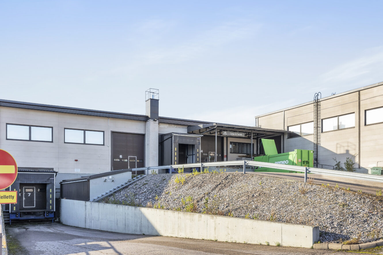 Kaupallisen varaston lastauslaiturialue, jossa on toimituslaitureita, kalteva ajotie ja suuri vihreä kontti kirkkaalla taivaalla.