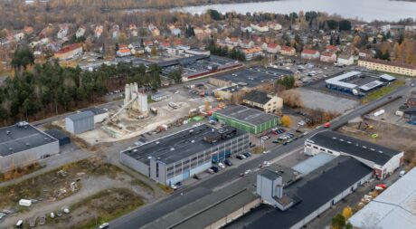 Ilmakuva teollisuusalueesta, jossa on useita rakennuksia, läheisiä asuintaloja ja joitakin puita syksyllä.