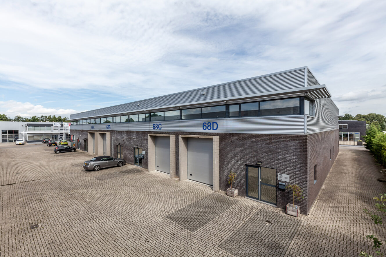 Modern industrieel gebouw met meerdere garagedeuren met de aanduidingen 68C en 68D, een benedenverdieping van baksteen, een bovenverdieping van metaal, buiten geparkeerde auto’s en een bestrate binnenplaats.
