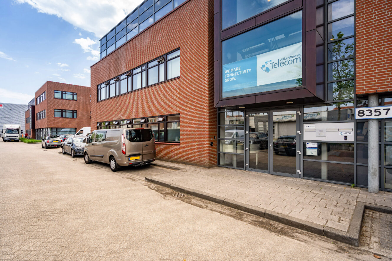 Een modern bakstenen kantoorgebouw met grote ramen, geparkeerde auto's en een bord met de tekst We make connectivity grow and Telecom boven de ingang.