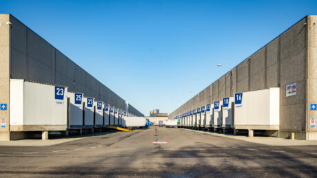 Een weids uitzicht op een laadperron met meerdere genummerde laadperrons aan beide zijden, onder een strakblauwe hemel.