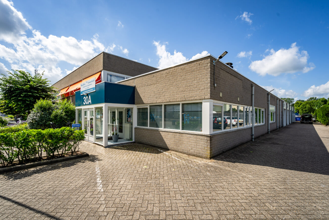 Een modern handelsgebouw van één verdieping met grote ramen en een blauw bord met het opschrift 30A, tegen een heldere, halfbewolkte lucht.