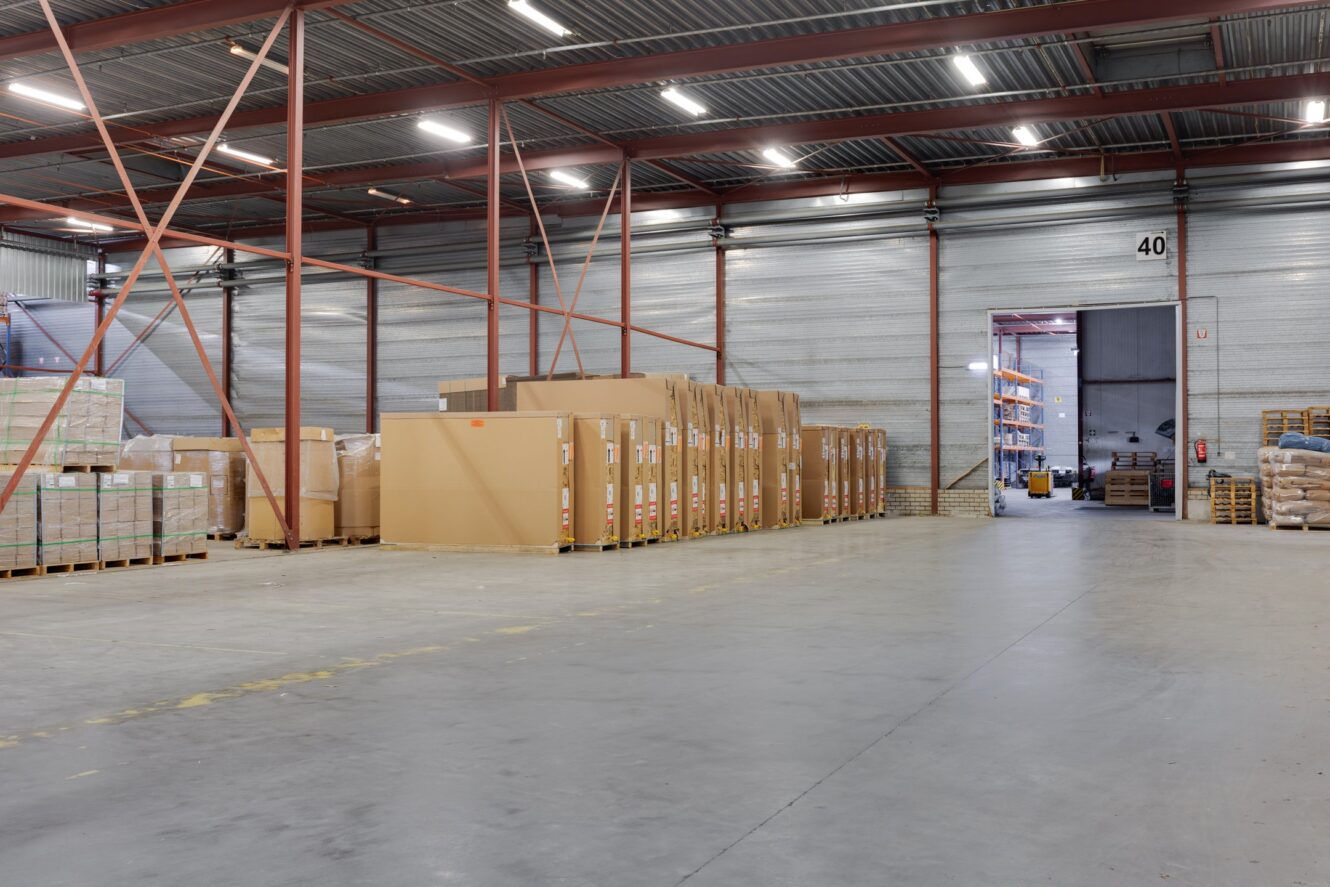 Groot magazijn binnen met stapels kartonnen dozen en pallets netjes gerangschikt bij een metalen muur en open deuropening met het label 40.