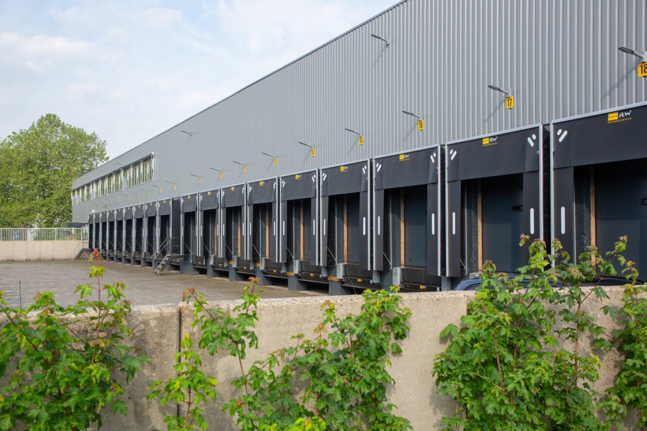 Een rij laadkades bij een groot industrieel magazijn, met genummerde baaien en een betonnen barrière op de voorgrond.