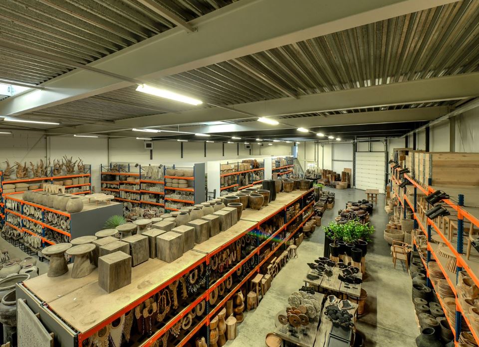 Magazijninterieur met hoge planken waar verschillende houten en keramische potten, plantenbakken en decoratieve voorwerpen staan, allemaal netjes georganiseerd en verlicht door plafondverlichting.