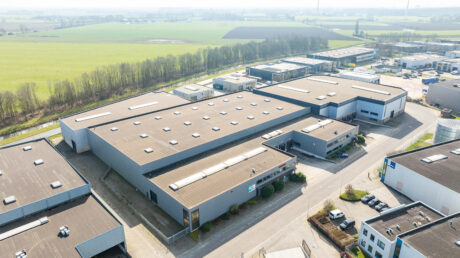 Luchtfoto van een industrieterrein met grote magazijngebouwen, parkeerplaatsen en omliggende groene velden.