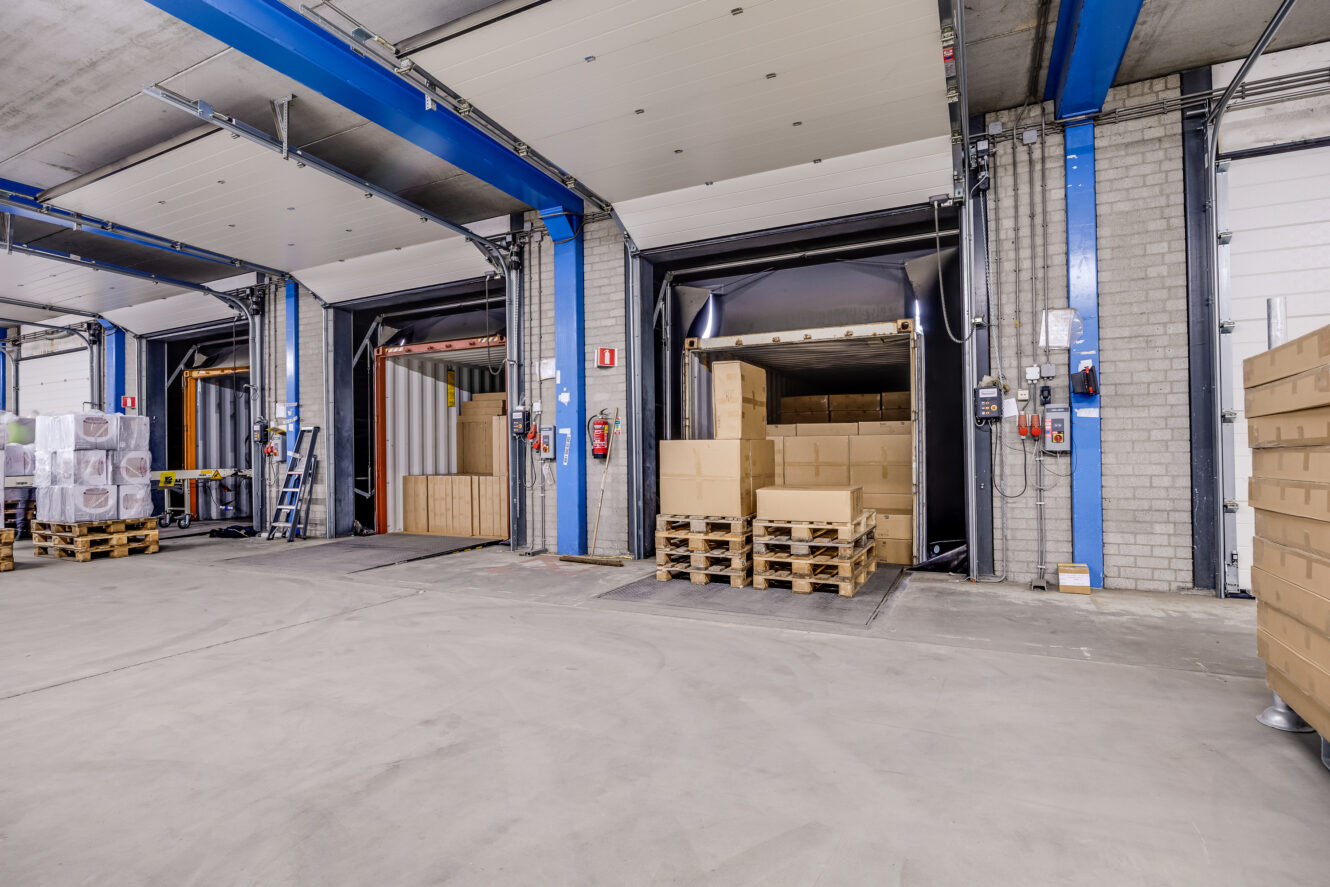 Laadperron met open deuren; pallets met kartonnen dozen worden in vrachtwagens geladen in een magazijn.