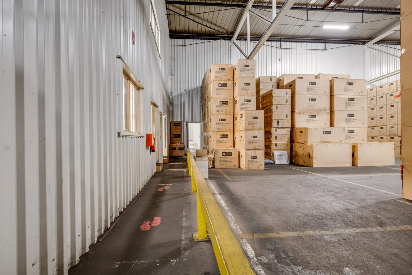 Stapels kartonnen dozen staan in rijen in een magazijn met betonnen vloeren en metalen muren.